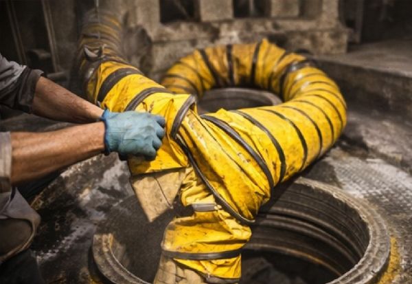 Worker setting up flexible ventilation duct into a manhole for confined space airflow control.