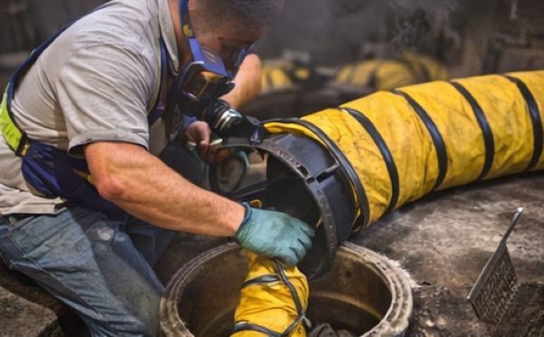 Worker setting up flexible ventilation duct into a manhole for confined space airflow control.